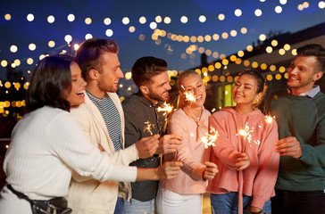 leisure, celebration and people concept - happy friends with sparklers at rooftop party at night...
