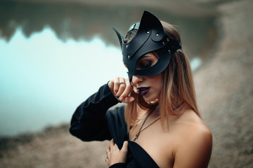 a woman in a black cat mask stands on the background of nature