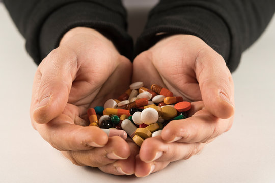Male hands holding high number of  pills on white blackground. High resolution image for pharmaceutical industry.