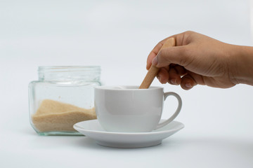 Hand put wooden spoon of sugar in white hot drink cup, white background