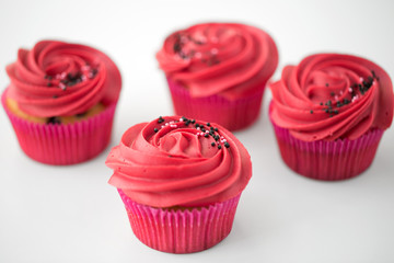 food, baking and pastry concept - close up of cupcakes or muffins with red buttercream frosting and sprinkles