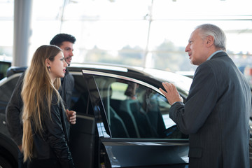 Happy young family talking to the salesman and choosing their new car in a showroom