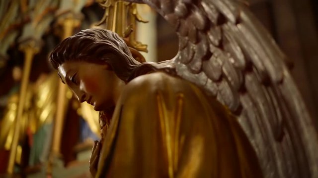 gilded statue of angel with large wings in a catholic church, close-up view, camera moving around