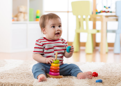 Cute baby playing with pyramid toy in nursery