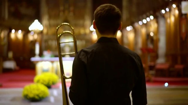 male trumpeter is standing in front of altar in church and playing trumpet, performing a concert