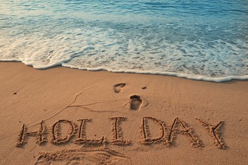 Concept HOLIDAY handwriting on sand beach with wave and blue ocean.
