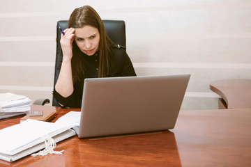 Puzzled business woman thinking hard concerned about online problem solution looking at laptop screen. Businesswoman trying to solve a difficult assignment  online in a desktop computer at office.