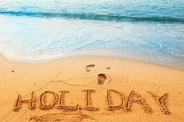 Concept HOLIDAY handwriting on sand beach with wave and blue ocean.