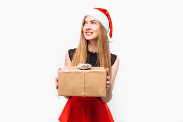 Happy young woman in santa hat and dress, celebrating new year, in her hands, christmas gift....