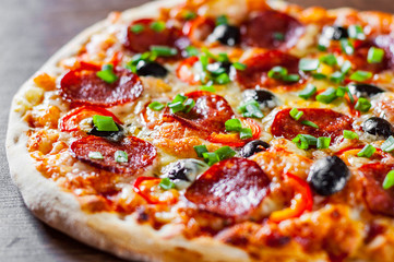Pizza with Mozzarella cheese, pepperoni, tomato, pepper, olive, salami. Italian pizza on wooden table background