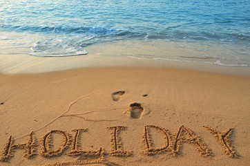 Concept HOLIDAY handwriting on sand beach with wave and blue ocean.