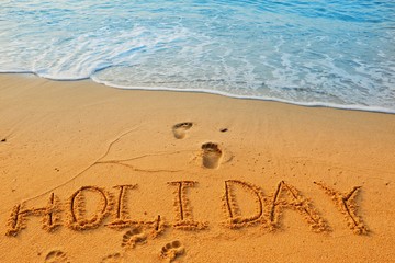 Concept HOLIDAY handwriting on sand beach with wave and blue ocean.