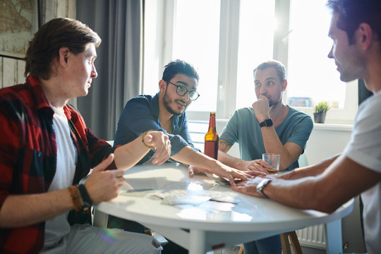 Young Man In Eyeglasses Take His Money While Playing In Poker With His Friends At The Table At Home