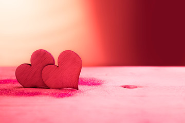 Two red hearts with glitter on pink table