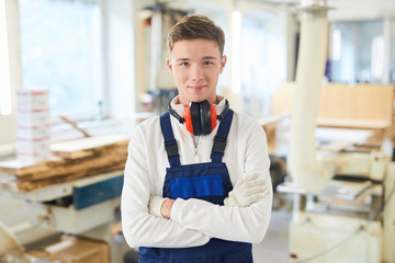 Content confident handsome young carpenter in ear protectors on neck wearing gloves and overall...