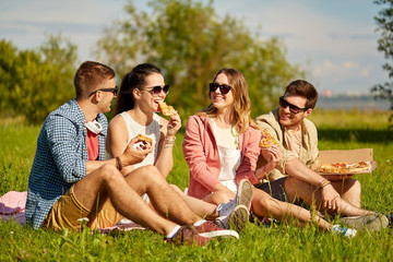 friendship, leisure and food concept - group of smiling friends eating pizza at picnic in summer park
