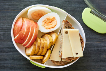 Lunch box with sandwich, egg and fresh fruit on a wooden table