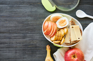 Lunch box with sandwich, egg and fresh fruit on a wooden table