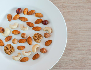Nuts, Almonds, Hazelnuts, Walnuts, Cashew Nuts On White Plate On A Wooden Table. Healthy Organic Snack, Breakfast, Food Ingredients. Flat Lay Top-Down Composition.