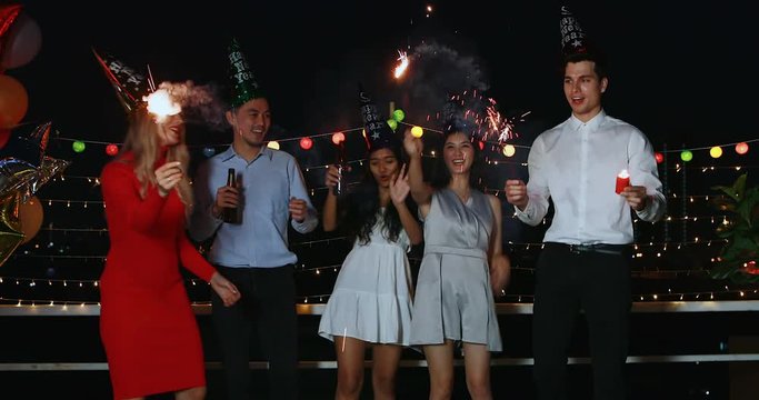 Group of Asian and Caucasian people in New year party , they holding bottle of alcohol in their hands, dancing and playing sparklers, concept for New Year party.