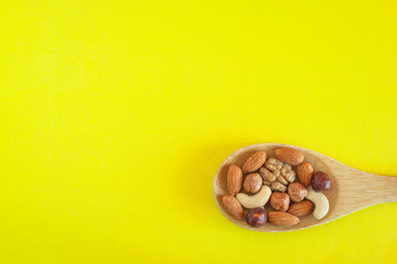 Assorted Nuts In A Wooden Spoon On Yellow Background. Healthy Organic Snack, Breakfast, Food Ingredients. Flat Lay Top-Down Composition.