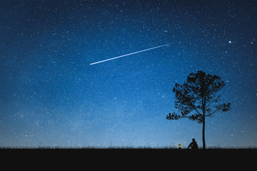 Silhouette of man sitting on mountain and night sky with shooting star. Alone concept.