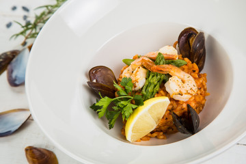 An overhead photo of a seafood risotto on teal textures, with a fork and a spoon, a glass of white wine, and a place for text