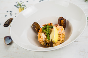 An overhead photo of a seafood risotto on teal textures, with a fork and a spoon, a glass of white wine, and a place for text