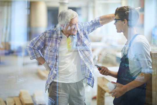 Furious emotional gray-haired mature carpenter foreman pointing with hand and yelling at lazy worker while dressing down him for poor performance in workshop