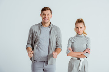 excited man with clenched fists and dissatisfied woman with arms crossed looking at camera isolated on grey
