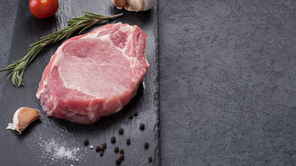 Raw bone steak with spices on a black stone. Top view. Copyspace