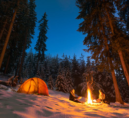 couple camping with campfire and tent outdoors in winter
