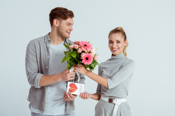 man greeting beautiful woman with Valentines card and flower bouquet isolated on grey