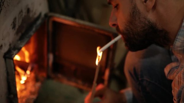 A man lighting a cigarette against a wooden stick
