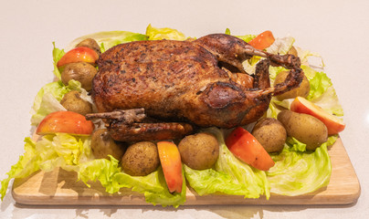 Christmas goose whole roasted and crispy on the cutting board with roasted potatoes, apples and brussels sprouts.