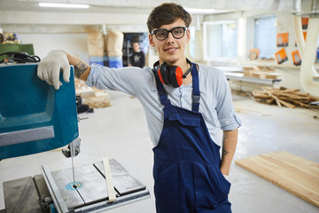 Smiling confident handsome young carpentry specialist wearing eyeglasses and ear protectors on neck...