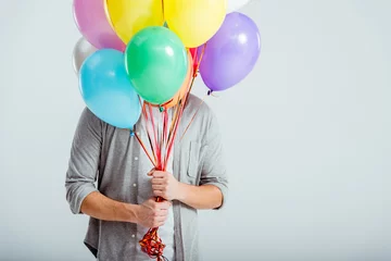 Foto op Canvas man in grey clothes hiding behind bundle of colorful balloons with copy space on grey background © LIGHTFIELD STUDIOS
