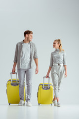 happy couple carrying yellow suitcases and looking at each other on grey background, travel concept