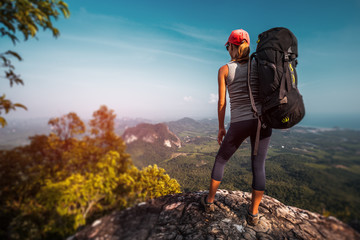 Woman hiker with big backpack stands on the rock and enjoys the valley view