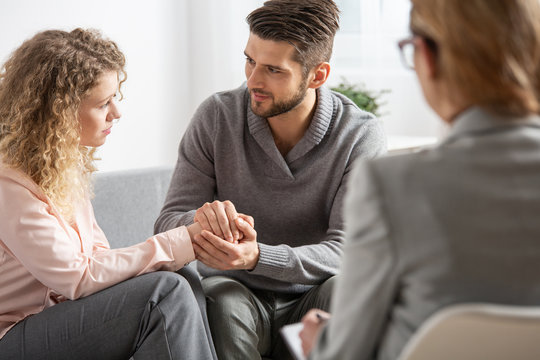 Young husband apologizing his worried wife during marital therapy with counselor