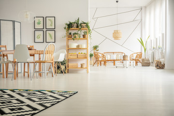 Geometric pattern on white wall in bright open plan interior with wooden table with chairs and rattan furniture in living room