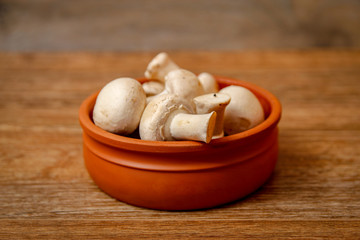 Fresh white champignon mushrooms in brown ceramic bowl on wooden vintage table