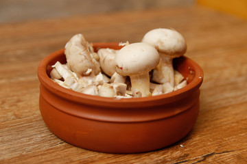 Fresh white champignon mushrooms in brown ceramic bowl on wooden vintage table