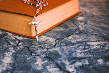 Silver rosary and cross resting on the closed book at gray table,front view.religion school concept.Vintage style.