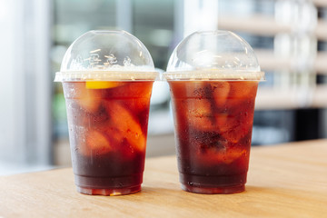 Two cups of Iced nitro cold brew coffee with lemon on wooden table with blur background.