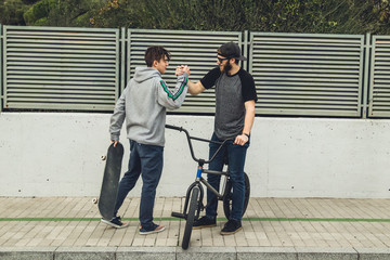 Young people riding bikes and skateboards in the city. Guys with a skate and a bmx down the street.