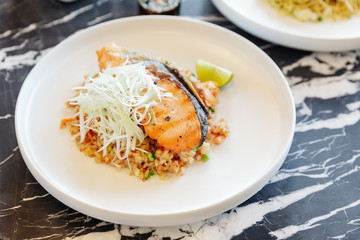 Garlic fried rice with grilled salmon served with chili bean sauce on black marble top table.
