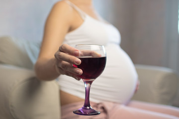 Pregnant woman with glass of red wine in hand indoors