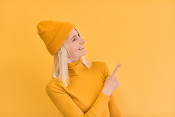 Studio image of happy smiling Caucasian woman with blonde hair indicates with fore finger at blank...