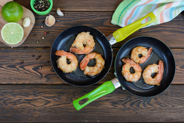 Delicious fried shrimps on a small pans next to each other and lime with garlic and pepper on a wooden background